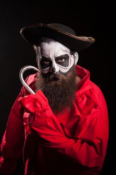 Man with long beard dressed up like a spooky pirate with a hook over black background.