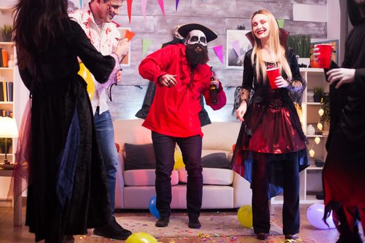 Bearded pirate holding a beer smiling while celebrating halloween with other scary monsters.