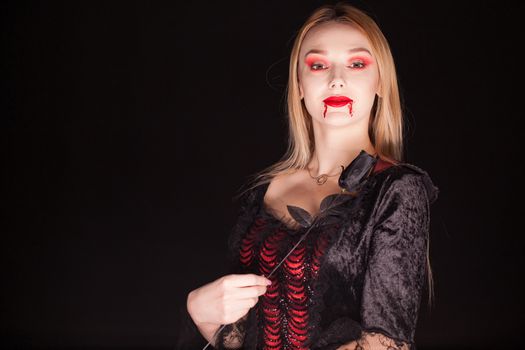 Woman wearing a vampire costume with a rose over black background.
