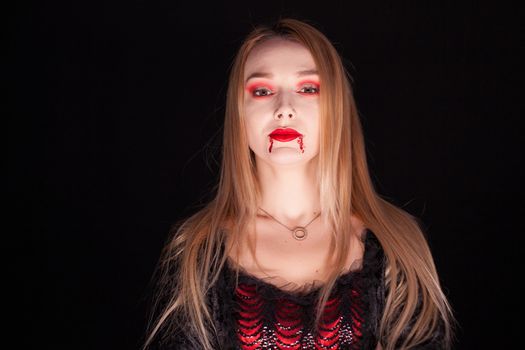 Beautiful blond woman dressed up like a vampire over black background.