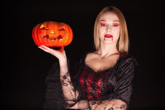 Beautiful blond woman dressed up like an evil vampire holding a pumpkin for halloween.