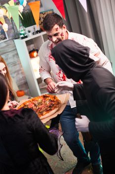 Rear view of people wearing halloween costumes excited about delicious pizza.