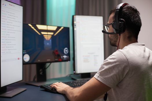 Man with eyeglasses wearing headphones while playing shooter games and reading streaming chats on dual screen setup