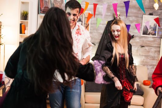 Man dressed up like a spooky zombie smiling at halloween celebration. Group of people having fun.