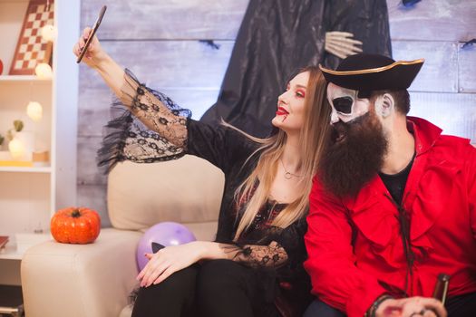 Medieval pirate winking while vampire woman taking a selfie at halloween party.