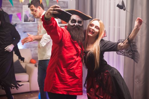 Happy vampire woman and pirate man taking a selfie at halloween celebration.
