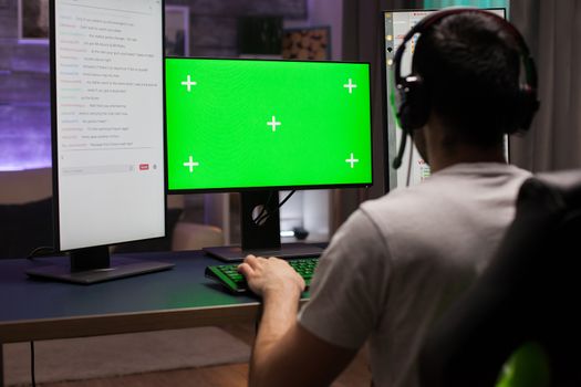 Back shot of competitive young man playing online games on computer with green mock up late at night.