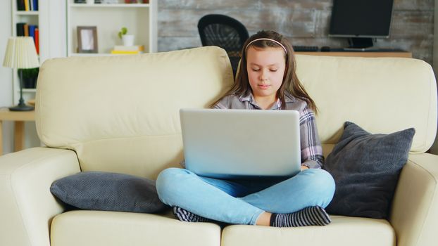 Sweet little girl with braces sitting on the couch using her laptop. Happy kid.