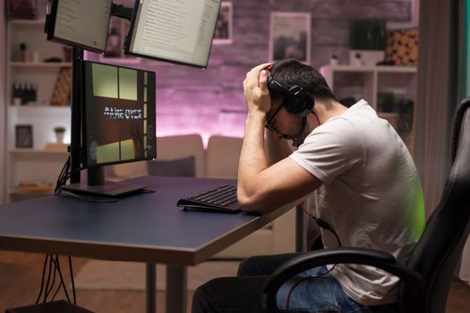 Side view of game over for man with headphones playing shooter games in room with neon light.