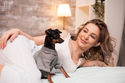 Relaxed young woman and her dog spending time in bed. Attractive woman in pajamas.