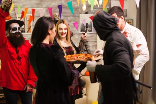 Group of friends excited about delicious pizza at halloween party.
