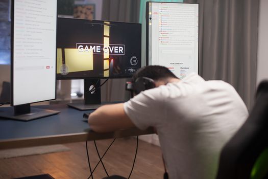 Disappointed young man keeping his head on the office because it's game over for him at online shooter games.