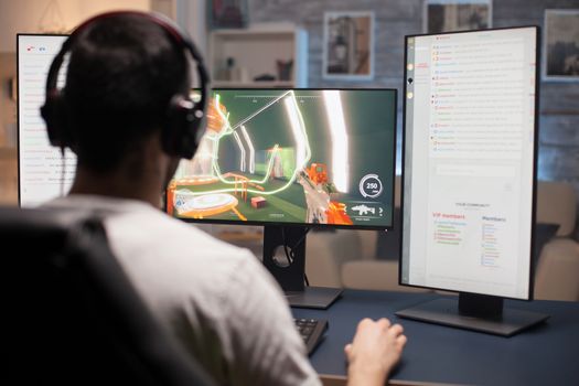 Back view of young man playing video games on computer with multiple monitors.