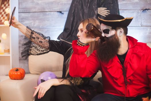 Beautiful woman in vampire costume taking a selfie with a pirate at halloween party.
