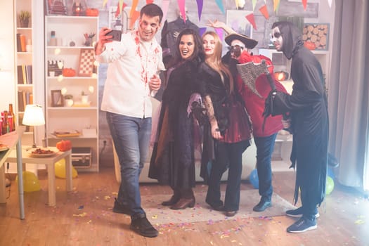 Cheerful group of young people taking a selfie in their costumes at halloween party.