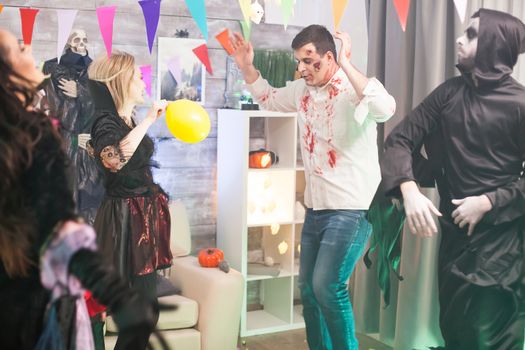 Bloody zombie and grim reaper dancing with hands up at halloween celebration.