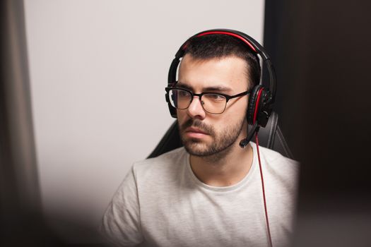 Portrait of young man with eyeglasses wearing headset while playing games on computer.