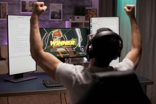 Excited young man with hands up after wining a competition of shooter games. Esport streaming.