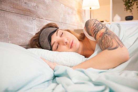 Beautiful woman with tattoo sleeping in bed at home with cover mask.