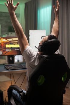 Young man full of joy with hands raised after his wining at online shooter game.