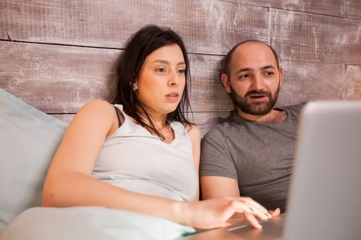 Young caucasian couple wearing pajamas surfing on the internet using laptop.