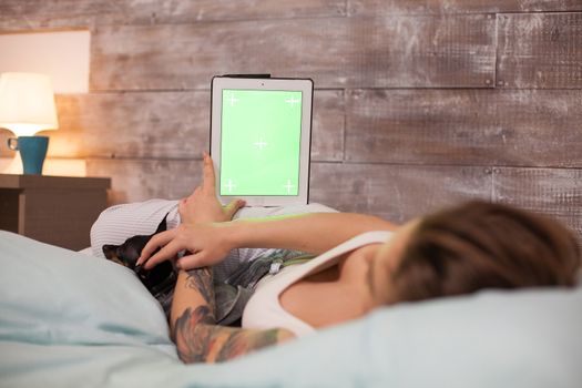 Bach shot of pretty woman wearing pajamas holding tablet computer with green screen next to her dog.