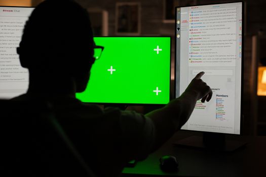 Back view of young man pointing at computer monitor while playing games in a dark room. Monitor with green screen.