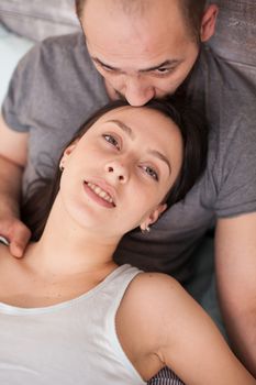 Top view of husband kissing his wife forehead after waking up in the morning.