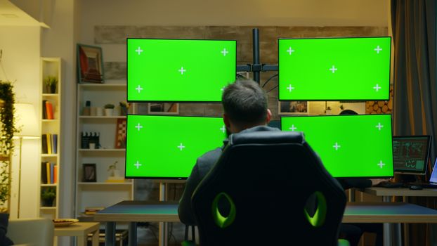 Back view of hacker using computer with multiple screen with green mockup.