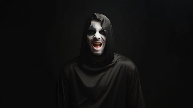Grim reaper with scary laughing over black background. Spooky costume.
