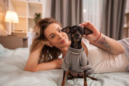 Caucasian pretty woman relaxing in bed wearing pajamas while playing with her little dog.