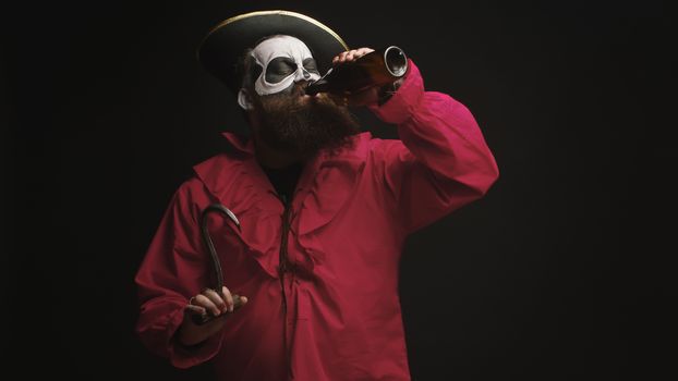 Drunk bearded man dressed up like a pirate with a hook for halloween over black background.