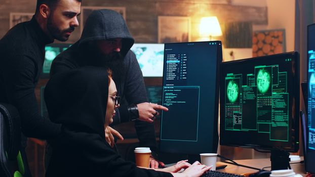 Team of hackers looking at computer with multiple monitors while committing cyber crimes.