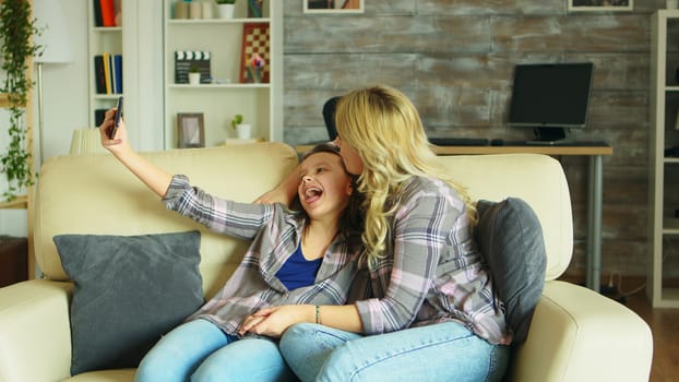 Cheerful mother and daughter taking a selfie with smartphone in living room.