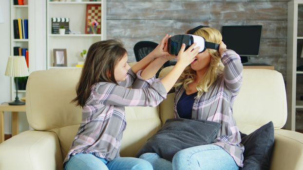 Little girl showing her beautiful mother how tu use virtual reality headset. Mother and daughter having fun.