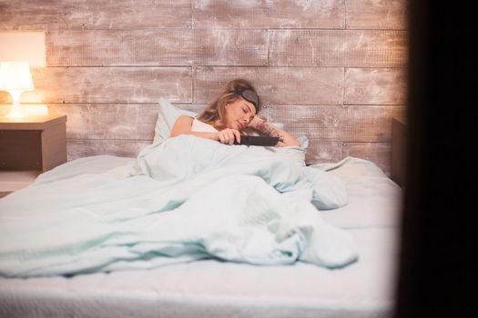 Beautiful young woman sleeping in bed holding tv remote control.