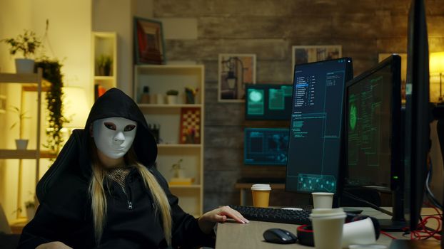 Hacker girl wearing a white mask to hide her identity. Looking into the camera.