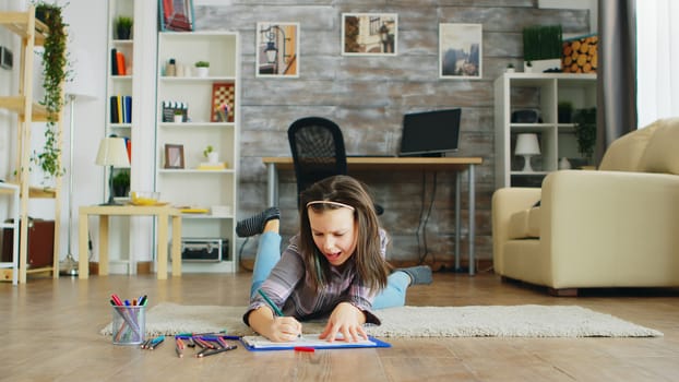 Happy little girl lying on the floor in living room drawing. Smart kid.