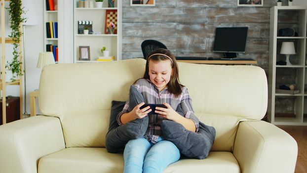 Excited little girl playing video games on her phone sitting on the couch.