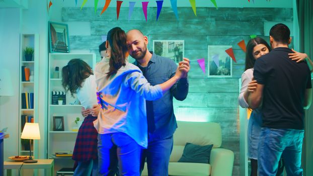 Group of couple dancing on slow music at a party with neon lights. Cheerful young men and women.