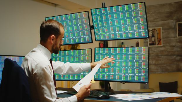 Bearded businessman in suit and tie checking his notes about stock market in home office.