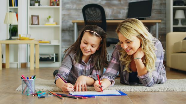 Cheerful little girl lying on the floor with her mother drawing.