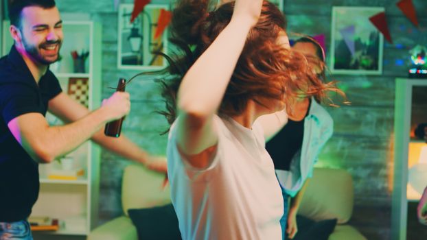 Care free beautiful young woman dancing at the party with her friends in a apartment with neon light.