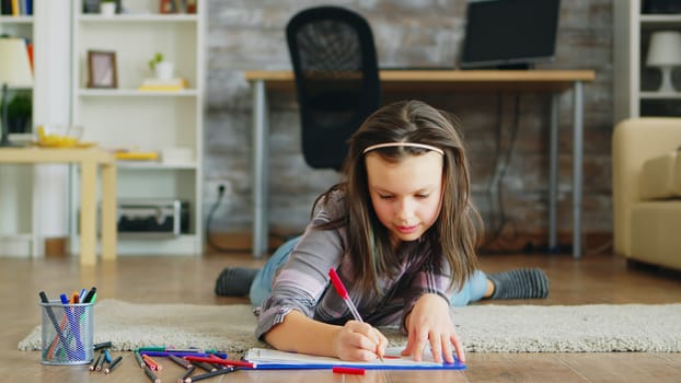 Cheerful little girl lying on the floor doing a creative drawing.