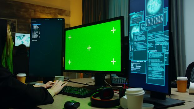 Zoom in shot of hacker girl in front of computer with green screen. Cyber criminal with hoodie.