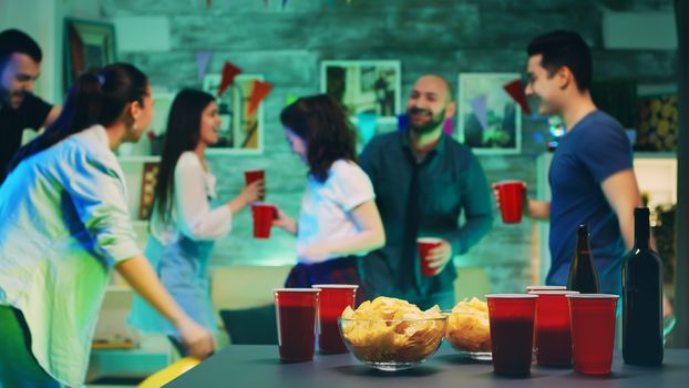 Chips and cups with beer on the table with people dancing in the background at the party.