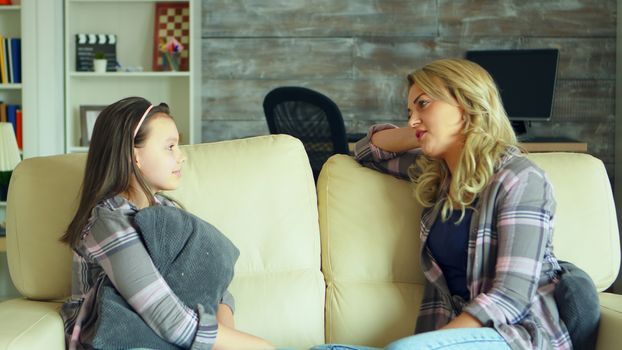 Preschool daughter sitting on the couch in living room talking with her mother.