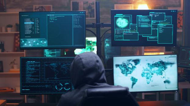 Back view of hooded cyber terrorist using super computer in dark room. Team of hackers.