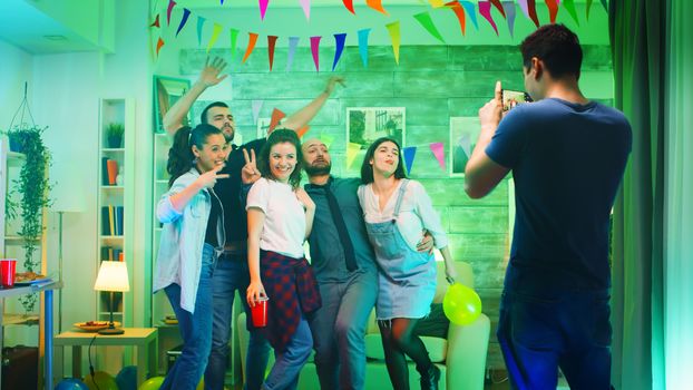 Cheerful group of people smiling at the party while young man takes photos of them.