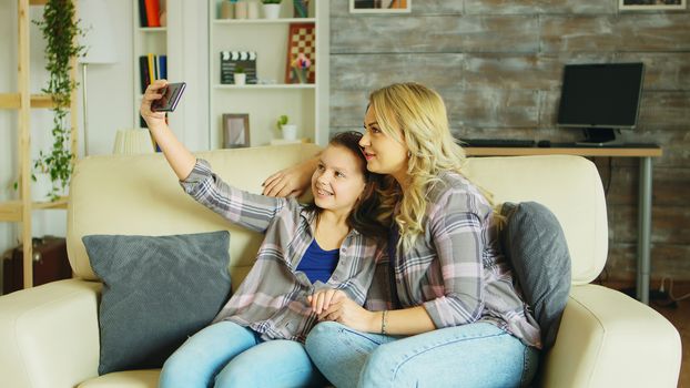 Little girl with braces sitting on the couch in living room taking a selfie with her mother.